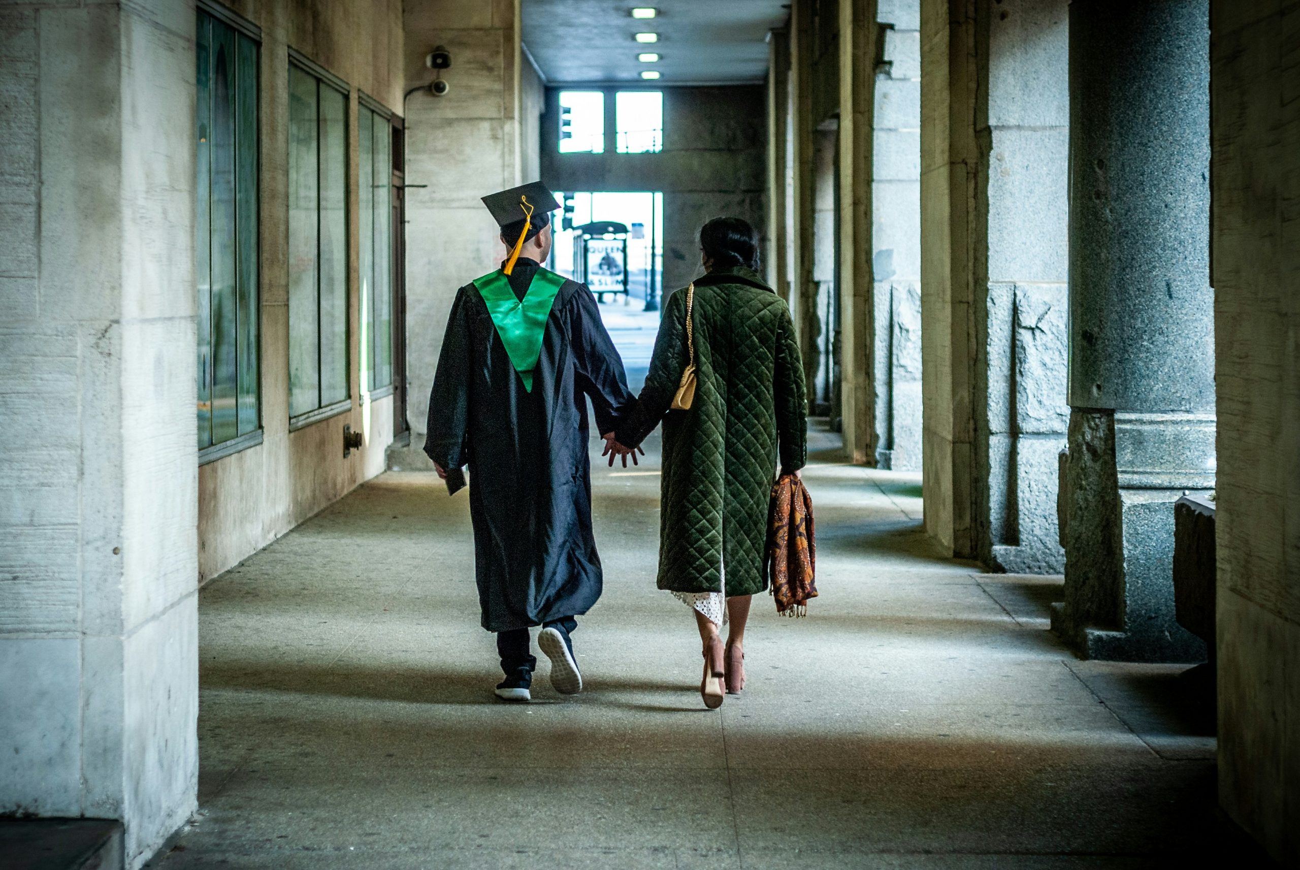 College graduate walking away from school in a soft lit alley.